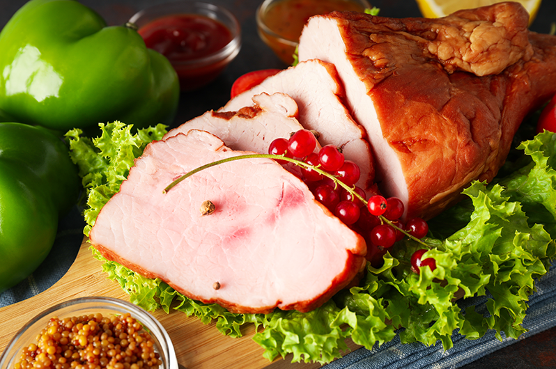 Cooked Ham cooked ham on a wooden plate surrounded by veggies