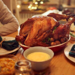 Happy African American woman enjoying in conversation with her friend while gathering for Thanksgiving at dining table.